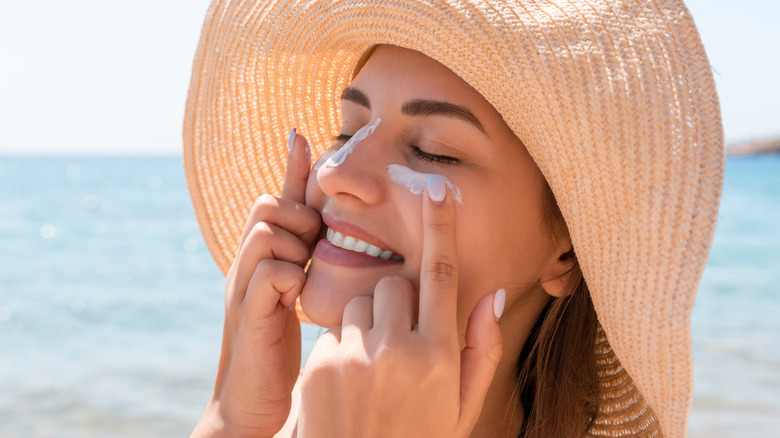 Woman on the beach applying sunscreen to her face