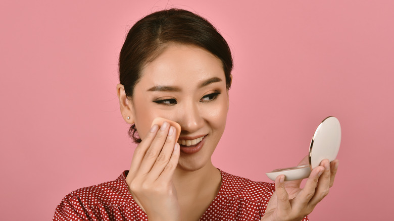 A smiling woman applying foundation 