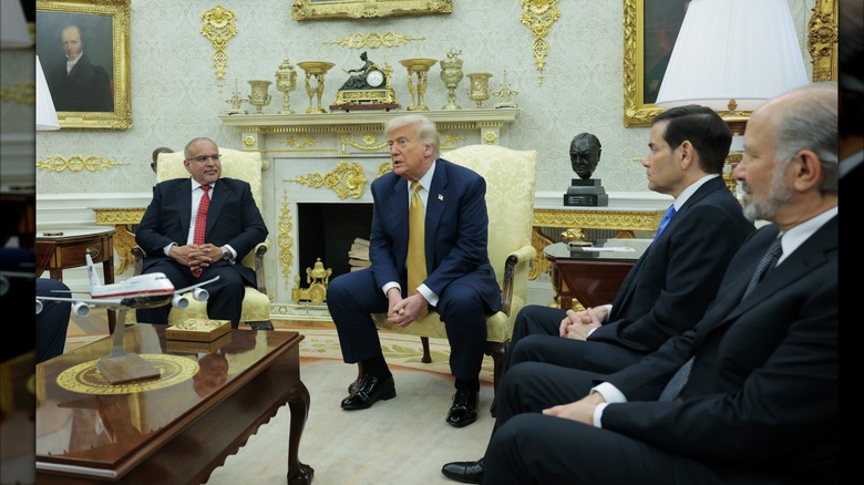 Donald Trump sitting in the oval office while wearing a suit and gold tie.