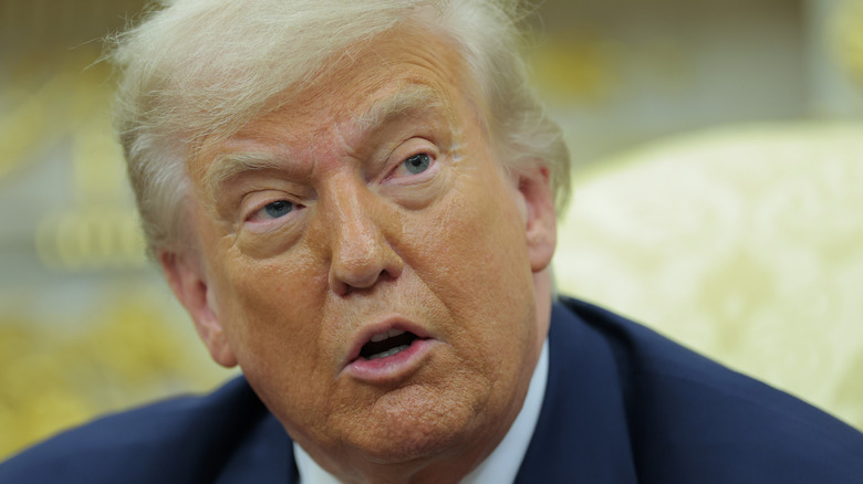 Donald Trump wearing a suit while speaking to reporters at the Oval Office.