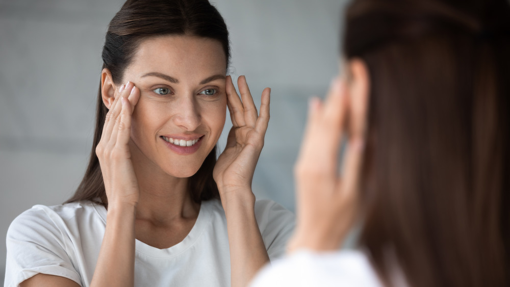 Woman applying eye cream in the mirror