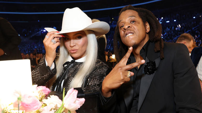 Beyonce tips a white cowboy hat, posing beside husband, Jay Z who flashes a peace symbol.
