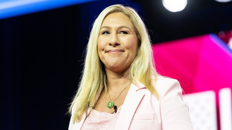 U.S. Rep. Marjorie Taylor Greene smilles in pink shirt and matching blazer with green and gold necklace