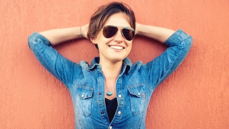 Young woman smiling and wearing sunglasses with her hands behind her head in a relaxed pose