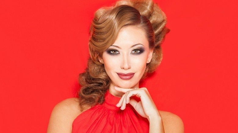 Woman wearing red lipstick and a red shirt while smiling against a red background
