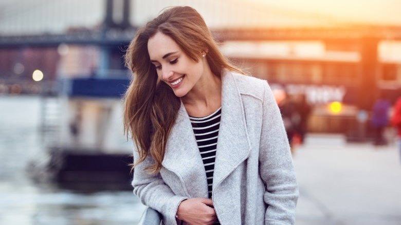 Young woman smiling while walking along a waterfront against the backdrop of a bridge