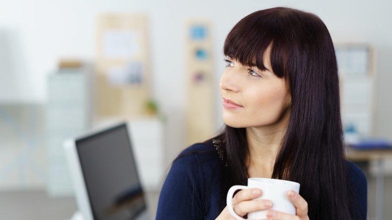 Young woman holding a mug and looking pensively off into the distance
