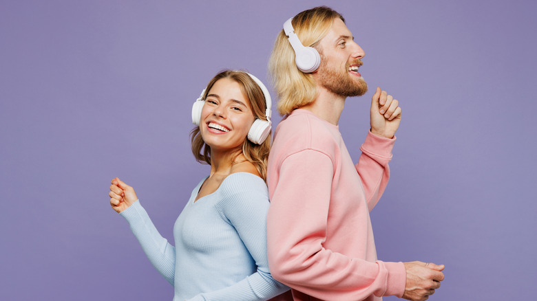 Blond couple with headphones standing back to back