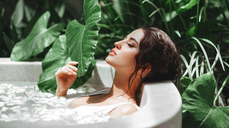 Woman relaxes in bathtub surrounded by plants