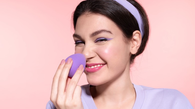 A smiling woman applying makeup with a blender 