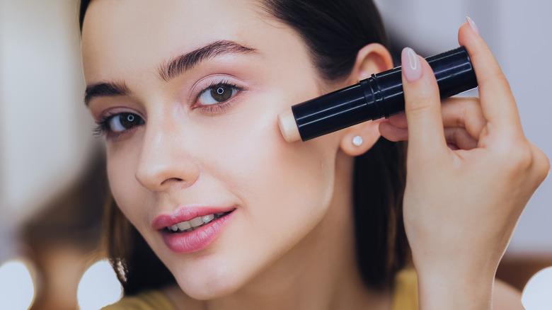 Woman applying stick foundation to face