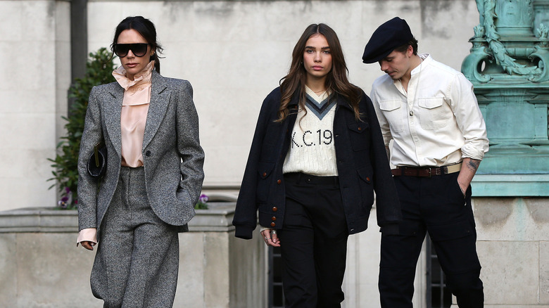 Victoria Beckham, Hana Cross, and Brooklyn Beckham walking on a street in London