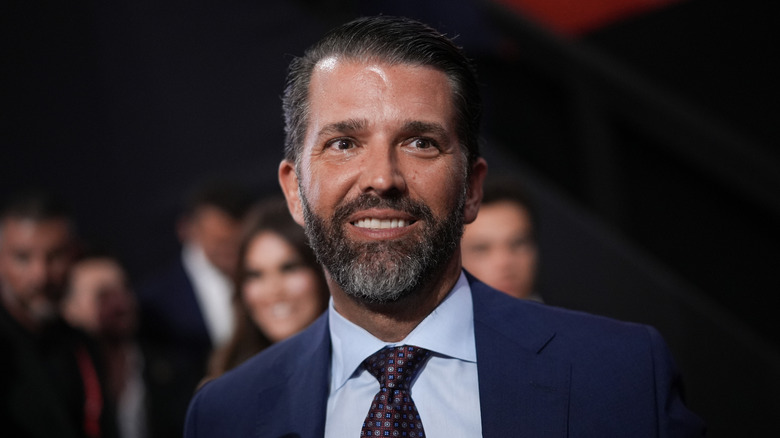 Donald Trump Jr. smiling in a navy suit