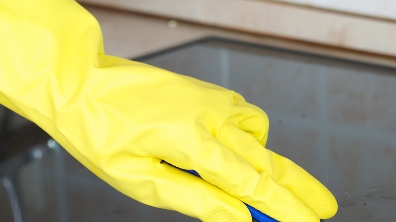 Person wearing yellow glove cleaning a glass stovetop.