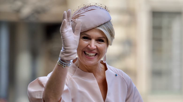Queen Máxima of the Netherlands smiles and waves in pink gloves, dress, and hat