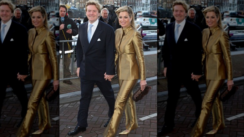 Queen Máxima and King Willem-Alexander holding hands and smiling as they walk past reporters and camera crew on the street
