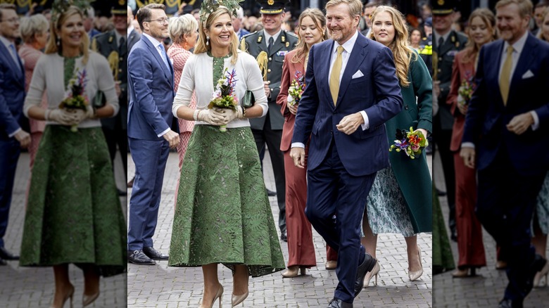 Queen Máxima and King Willem-Alexander smile on King's Day as she holds flowers outside in a green dress.