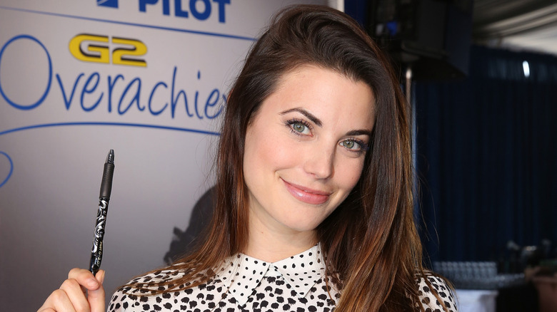 Meghan Ory smiling while holding up a pen