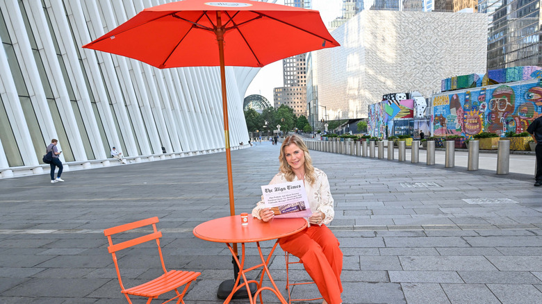 Alison Sweeney sits at a table and holds a newspaper