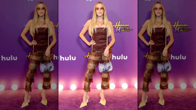 Alex Cooper posing in a brown tube top and patterned pants embellished with fringe.