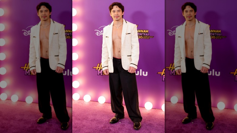 David Archuleta posing shirtless in a white jacket and black pants.