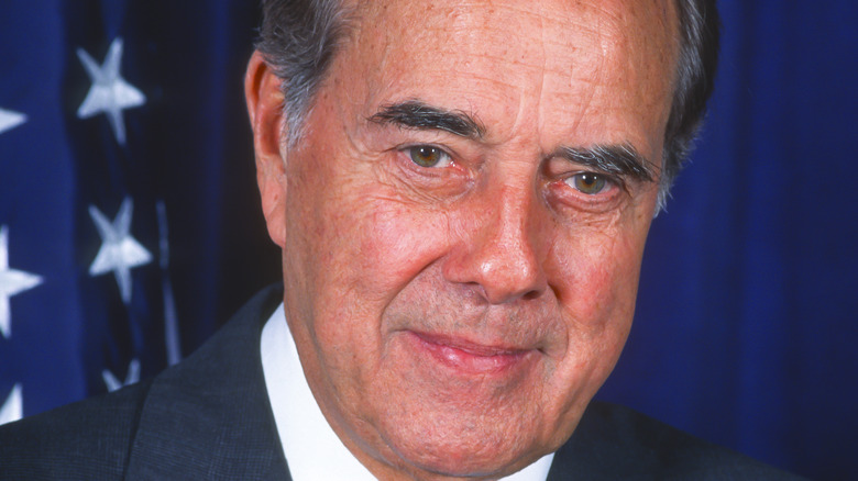 Senator Bob Dole poses with a smile next to an American flag.