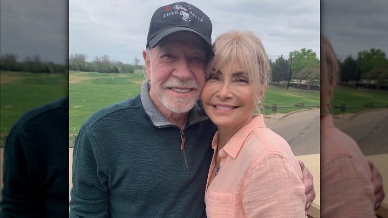 Gena O'Kelley and Chuck Norris smiling and posing cheek-to-cheek on golf course
