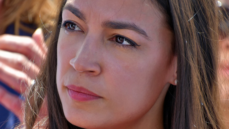 Alexandria Ocasio-Cortez looks off to the side with a pensive glance.