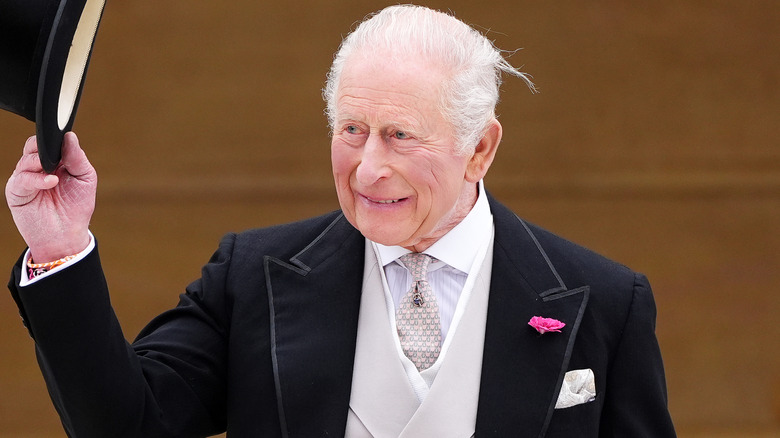 King Charles III smiling and holding up a top hat