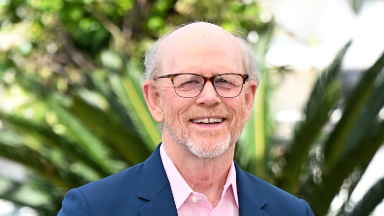 Ron Howard smiling in an open-collared light pink shirt with a navy blazer over it