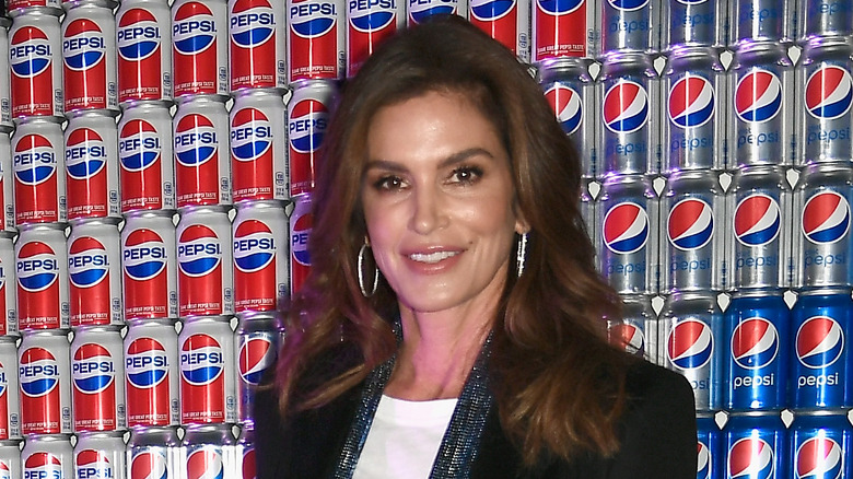 Cindy Crawford smiling in front of a wall of Pepsi cans