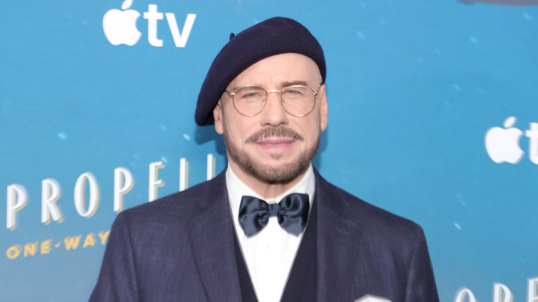 John Travolta posing in a navy blue suit with a matching beret and bow tie, and glasses