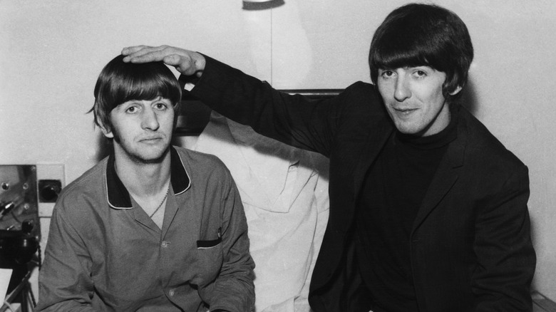 George Harrison touching the top of Ringo Starr's head as they pose for a photo together