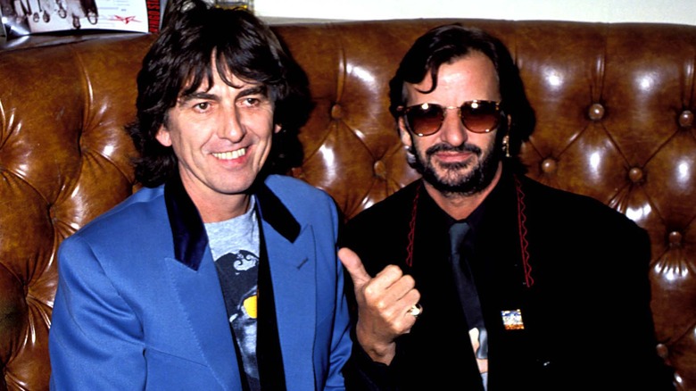 Ringo Starr gesturing at George Harrison with his thumb as they pose for a photo together