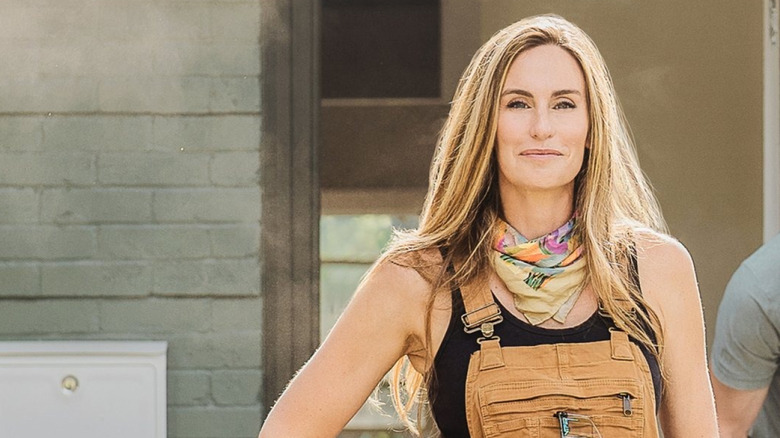 Kim Wolfe smirking with hand on hip with man lifting something behind her