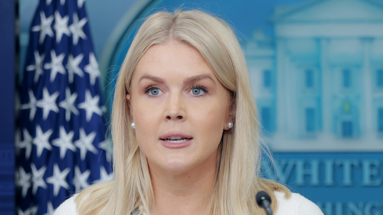 Karoline Leavitt speaking in a white sweater at a press conference.