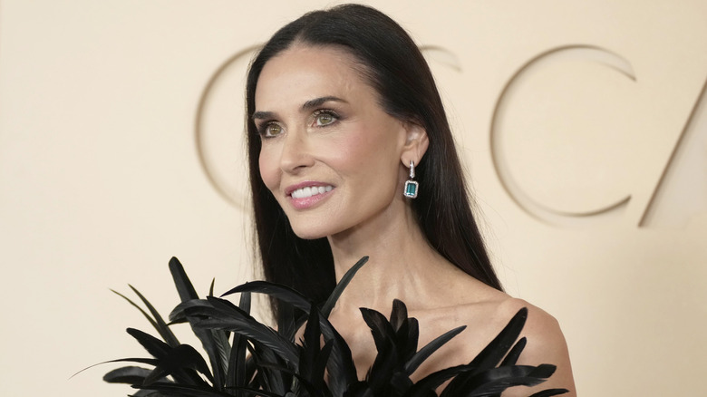 Demi Moore smiling while posing in a black feathered dress