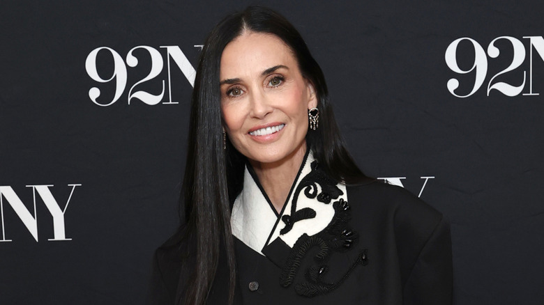 Demi Moore smiling while posing at an event in a black jacket with white detailing