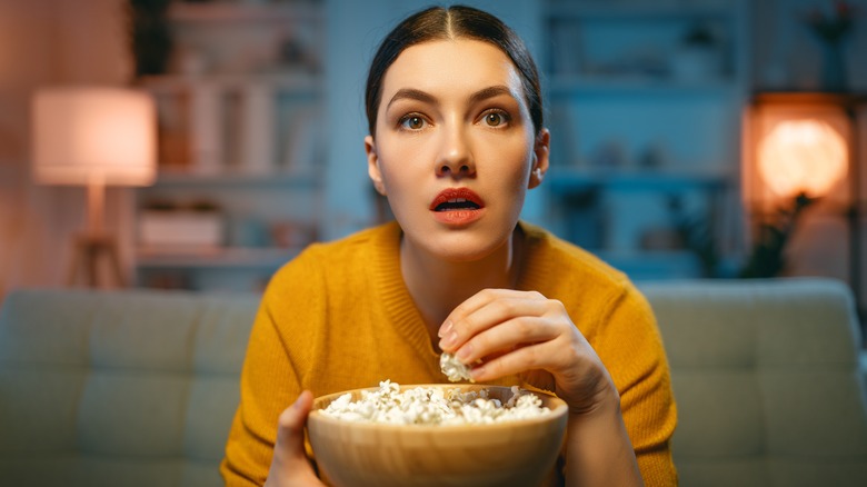 A woman eating popcorn and watching a movie.
