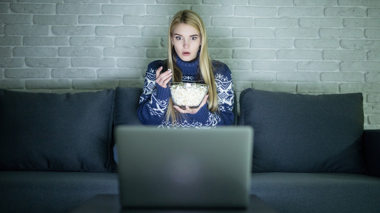 Woman watching movie on laptop, looking surprised