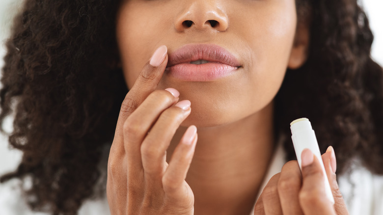 Woman applying lip balm, holding lip balm stick and applying with her finger