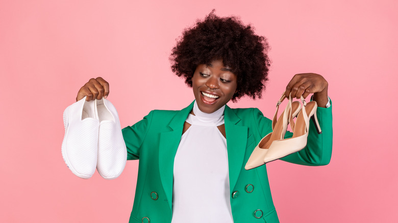 Woman holds up a pair of heels and a pair of flat shoes