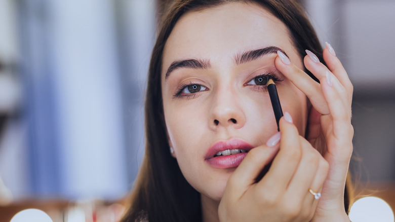 Woman applies eyeliner pencil