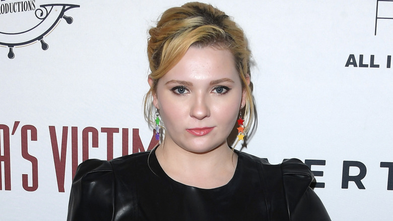 Abigail Breslin posing at an event in a black dress with her hair up