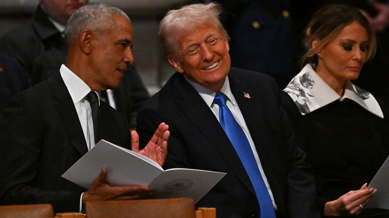 Donald Trump smiling while sitting next to Barack Obama