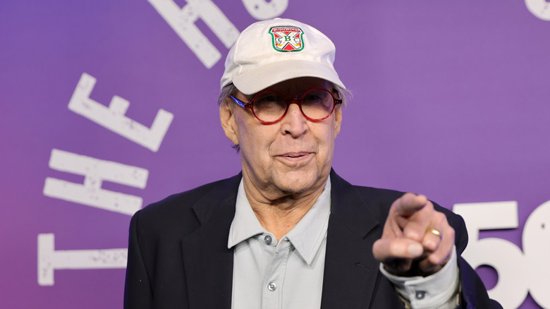 Chevy Chase wearing a baseball cap and pointing