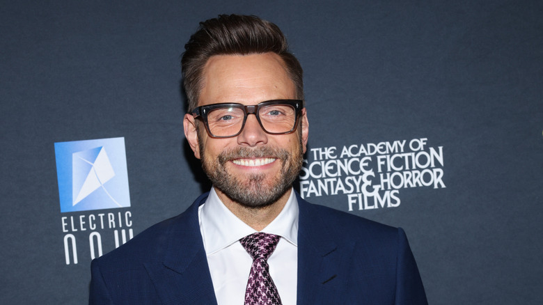 Joel McHale posing in front of a blue-grey background