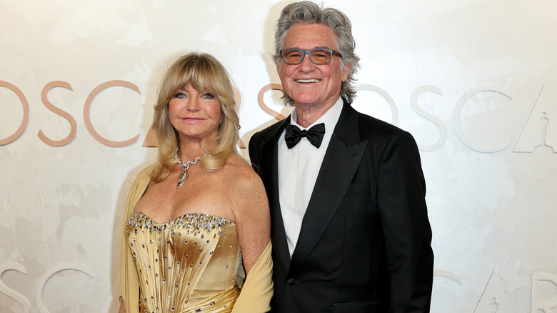 Goldie Hawn wearing a strapless gold dress and posing beside Kurt Russell in a tux at the 2025 Oscars