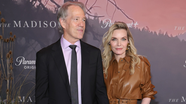 Michelle Pfeiffer wearing a brown leather belted top and posing next to David E. Kelley at a premiere event for The Madison