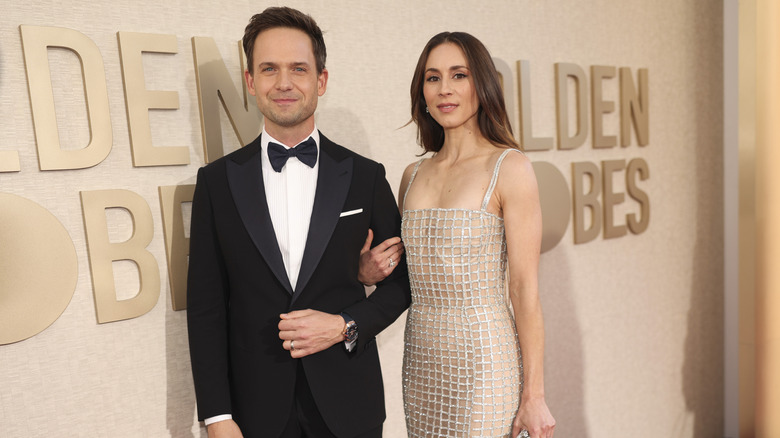Troian Bellisario wears a beige dress with a silver grid pattern and links arms with Patrick J. Adams, who is wearing a tux.